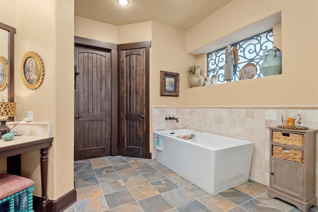 bathroom with a washtub, a textured ceiling, and tile walls