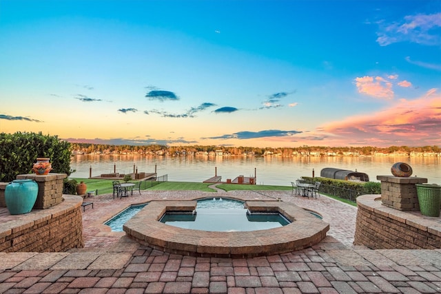 pool at dusk featuring a water view, an in ground hot tub, and a patio