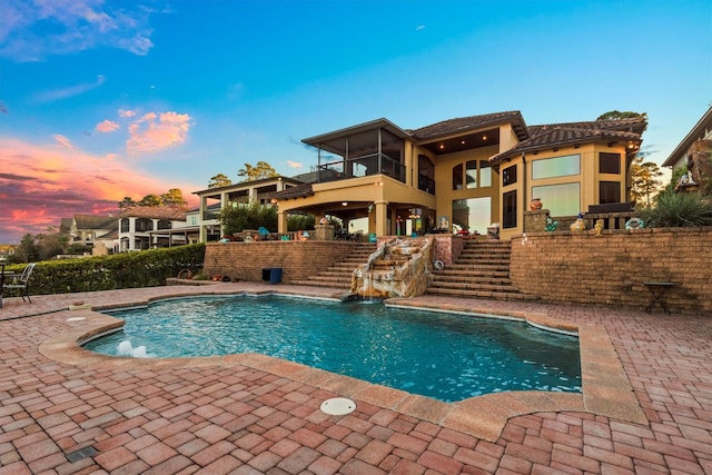 pool at dusk featuring a patio area, pool water feature, and an outdoor bar