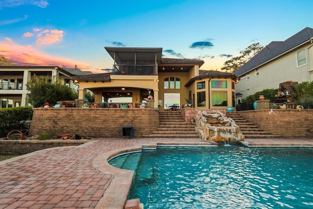 back house at dusk with a fenced in pool, a patio, and a sunroom