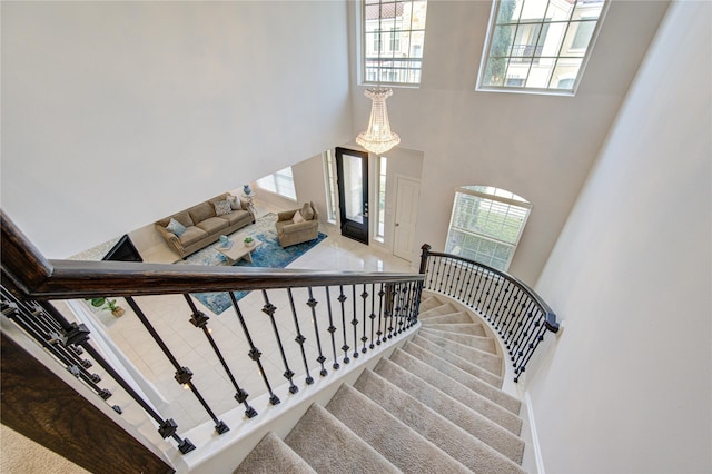 stairs with a towering ceiling, a chandelier, and carpet flooring