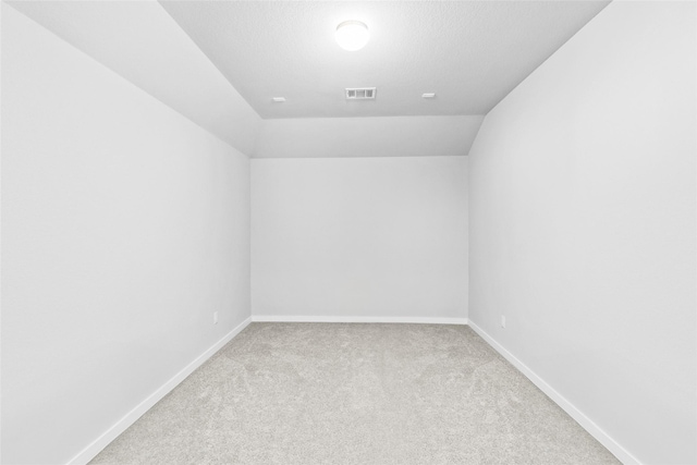 carpeted empty room featuring baseboards, visible vents, vaulted ceiling, and a textured ceiling