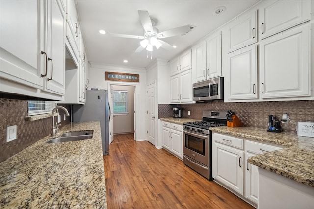 kitchen with light wood-style flooring, a sink, stainless steel appliances, white cabinetry, and backsplash