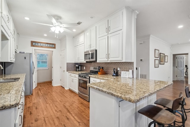kitchen featuring decorative backsplash, light wood-style flooring, a peninsula, stainless steel appliances, and white cabinetry