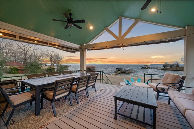 deck at dusk featuring outdoor dining area, a water view, and ceiling fan