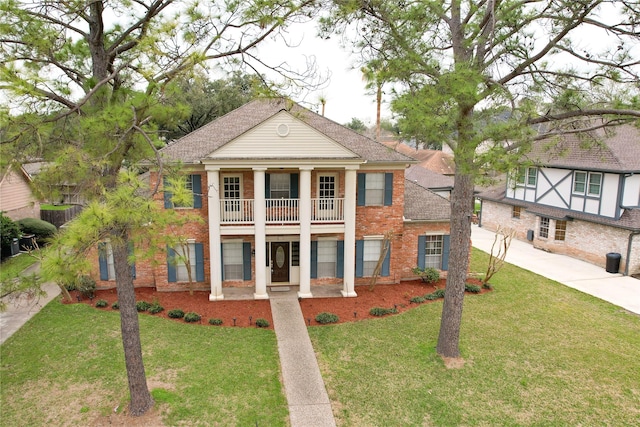 greek revival inspired property with a balcony, brick siding, concrete driveway, roof with shingles, and a front yard