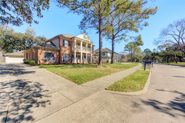 greek revival inspired property featuring a balcony, brick siding, a garage, and a front yard