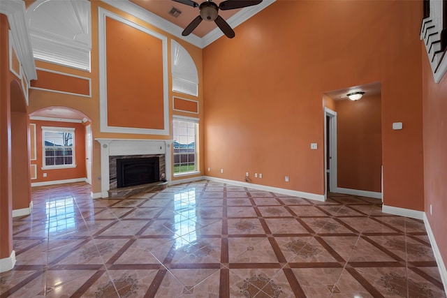 unfurnished living room featuring crown molding, a stone fireplace, ceiling fan, and a towering ceiling