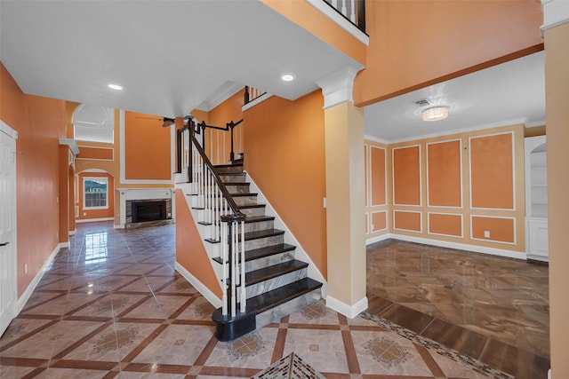 staircase featuring decorative columns, ornamental molding, and a towering ceiling