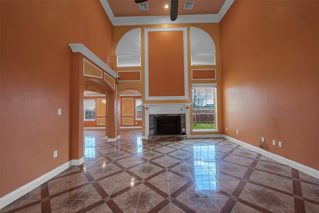 unfurnished living room with crown molding, a stone fireplace, and a towering ceiling