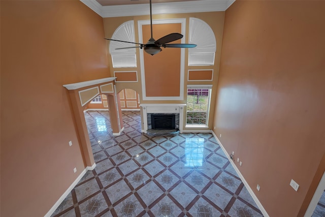 unfurnished living room featuring crown molding, a towering ceiling, and ceiling fan