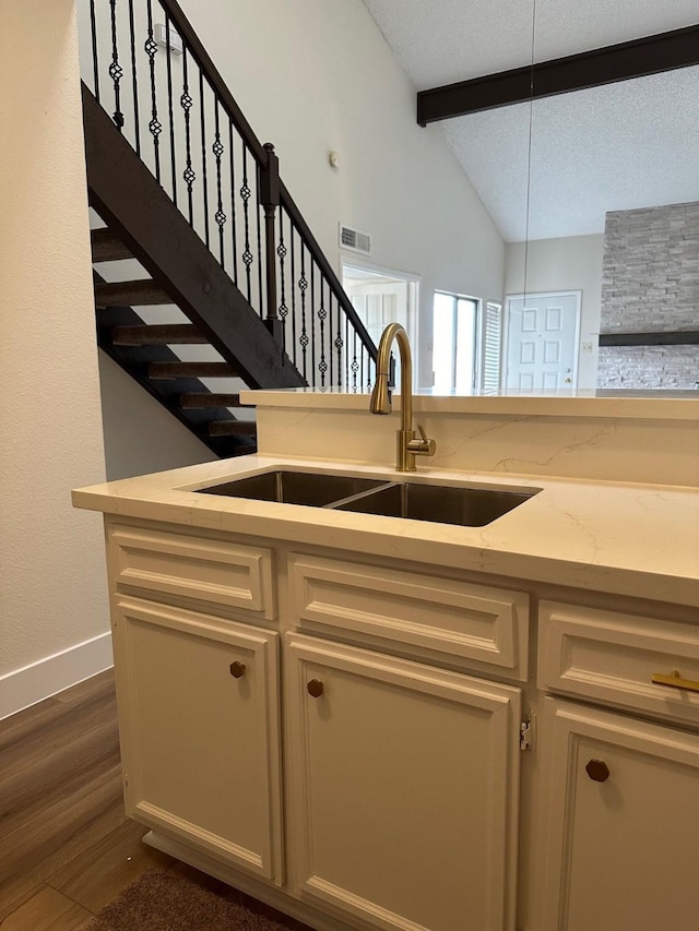 kitchen featuring light stone counters, dark wood finished floors, visible vents, lofted ceiling with beams, and a sink