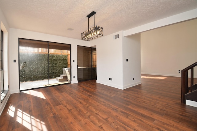 empty room with wood finished floors, visible vents, stairs, a textured ceiling, and a chandelier