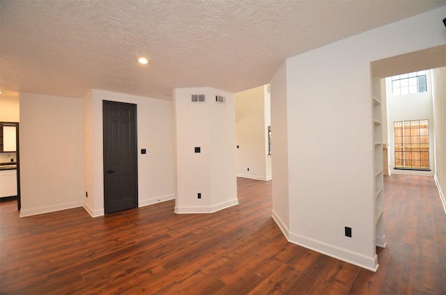 spare room featuring dark hardwood / wood-style flooring, built in shelves, and a textured ceiling