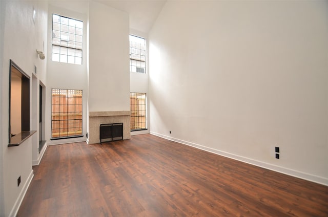 unfurnished living room featuring a tiled fireplace, baseboards, dark wood-type flooring, and a towering ceiling