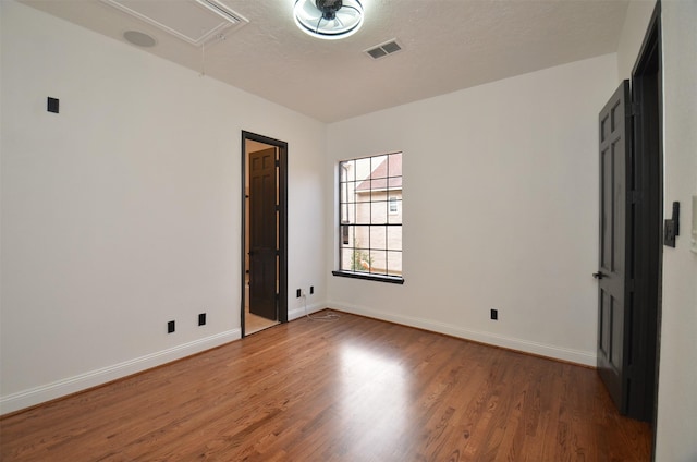 empty room featuring visible vents, attic access, baseboards, and wood finished floors