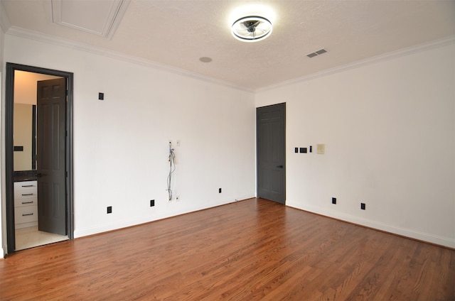 empty room with crown molding, wood finished floors, visible vents, and baseboards