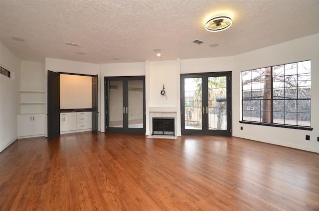 unfurnished living room featuring french doors, a textured ceiling, visible vents, and wood finished floors