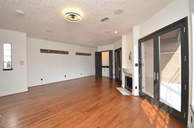 spare room featuring a fireplace with flush hearth, wood finished floors, visible vents, and a textured ceiling