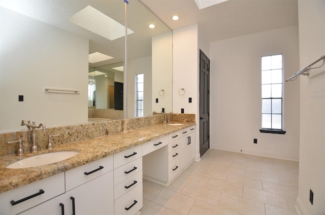 full bath with double vanity, a skylight, baseboards, and a sink