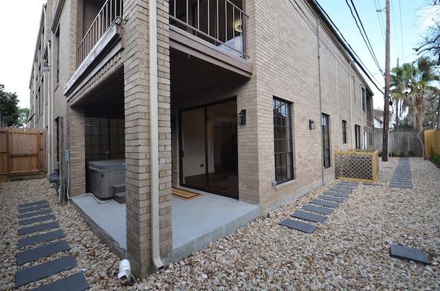 view of side of property with brick siding, a balcony, a patio, and a fenced backyard