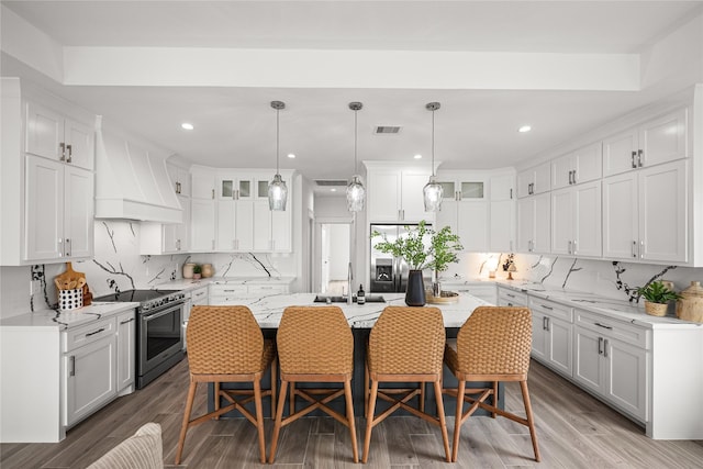 kitchen with white cabinetry, stainless steel appliances, premium range hood, and a center island with sink