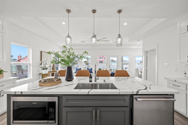 kitchen featuring built in microwave, sink, white cabinets, light stone countertops, and a center island with sink