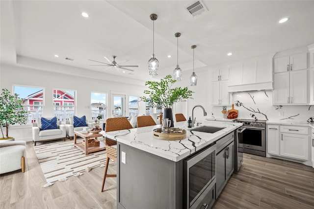 kitchen with pendant lighting, sink, appliances with stainless steel finishes, white cabinets, and a center island with sink