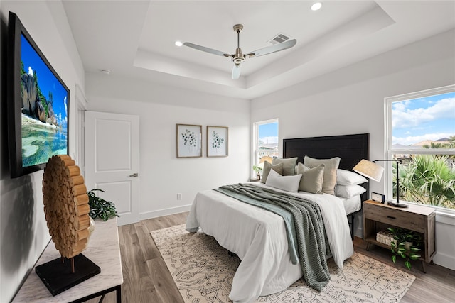 bedroom featuring ceiling fan, a raised ceiling, and light wood-type flooring