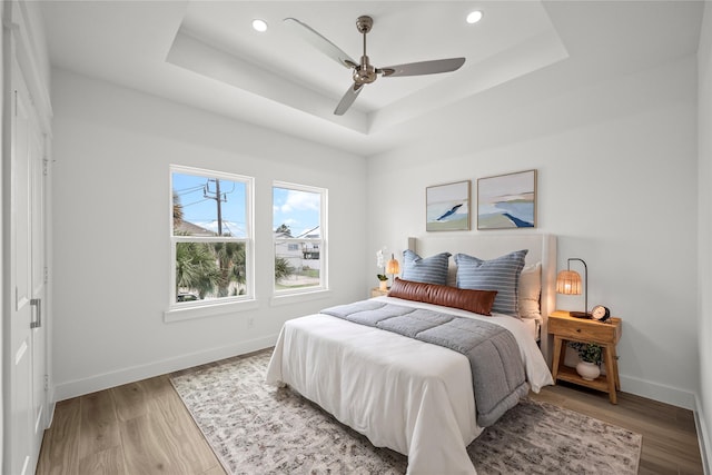 bedroom featuring light hardwood / wood-style flooring, ceiling fan, and a tray ceiling