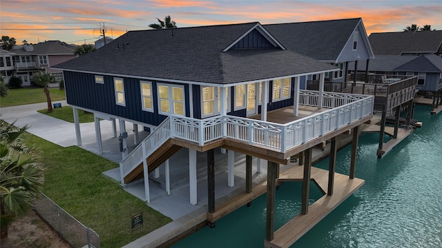 rear view of house with board and batten siding, roof with shingles, a water view, and stairway