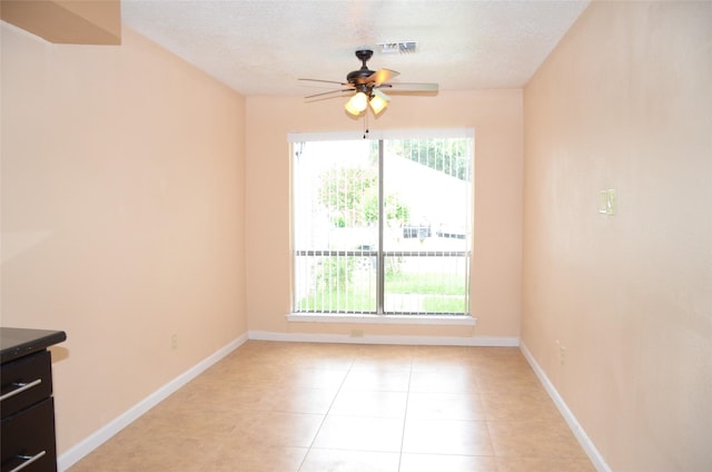 empty room with ceiling fan, a textured ceiling, a healthy amount of sunlight, and light tile patterned flooring