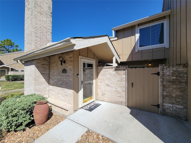 property entrance with board and batten siding, a gate, brick siding, and a chimney