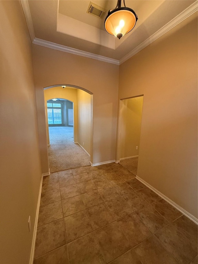 hall with ornamental molding, a raised ceiling, and tile patterned flooring