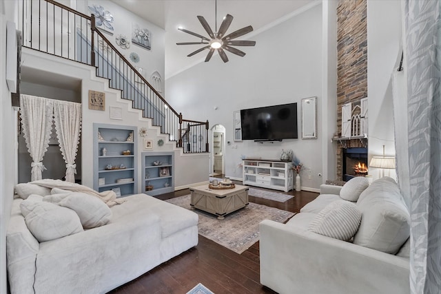 living room with dark hardwood / wood-style floors, a towering ceiling, built in features, a fireplace, and crown molding