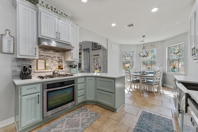 kitchen featuring tasteful backsplash, decorative light fixtures, green cabinets, stainless steel appliances, and white cabinets