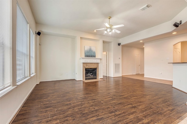 unfurnished living room featuring a tiled fireplace, dark wood-type flooring, and ceiling fan