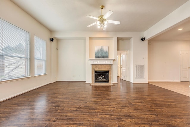 unfurnished living room featuring a tiled fireplace, dark hardwood / wood-style floors, and ceiling fan