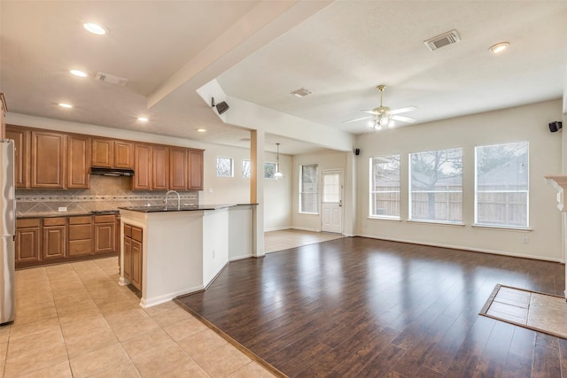 kitchen with stainless steel fridge, ceiling fan, tasteful backsplash, an island with sink, and light wood-type flooring