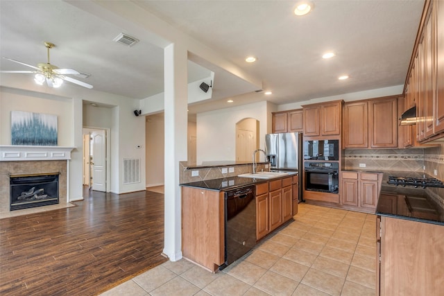 kitchen featuring sink, a tile fireplace, black appliances, decorative backsplash, and dark stone counters