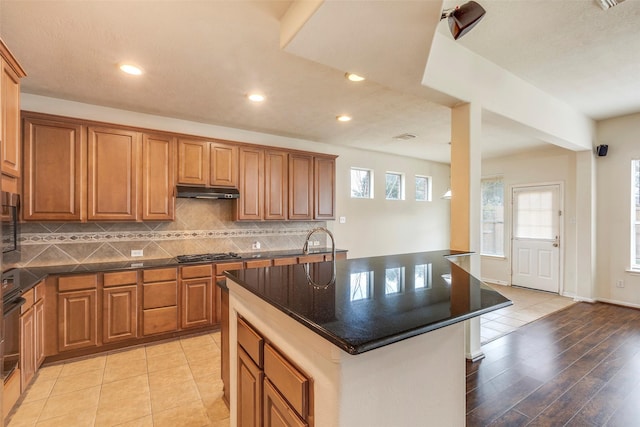 kitchen with stainless steel gas stovetop, light tile patterned floors, a center island with sink, and backsplash