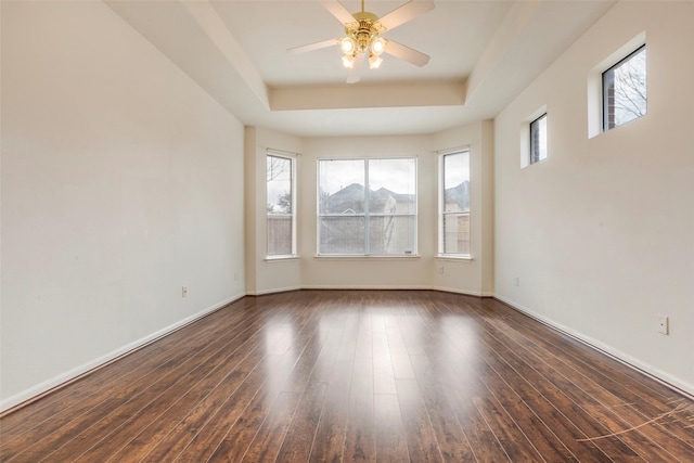 spare room with dark wood-type flooring, a raised ceiling, and ceiling fan