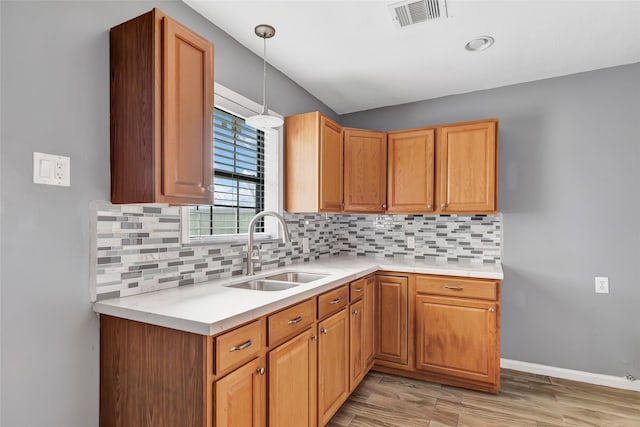 kitchen featuring hanging light fixtures, tasteful backsplash, sink, and light hardwood / wood-style flooring