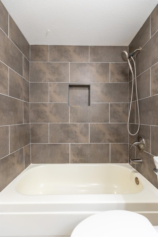 bathroom with tiled shower / bath combo, a textured ceiling, and toilet