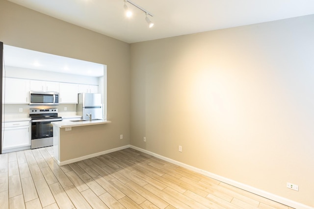 kitchen featuring white cabinetry, sink, kitchen peninsula, stainless steel appliances, and light wood-type flooring