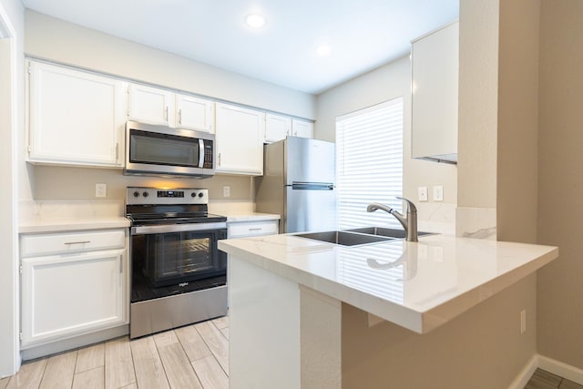 kitchen with white cabinetry, sink, kitchen peninsula, stainless steel appliances, and light stone countertops