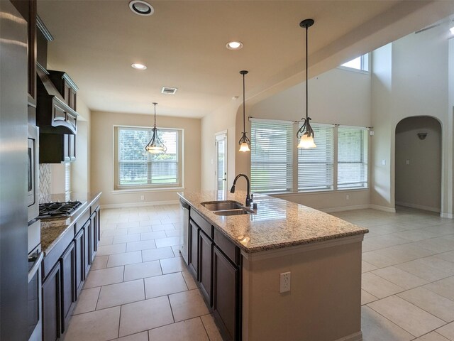 kitchen with pendant lighting, an island with sink, sink, light stone countertops, and dark brown cabinets