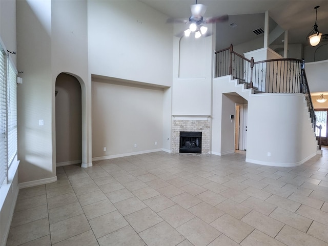 unfurnished living room with light tile patterned flooring, ceiling fan, a tile fireplace, and a towering ceiling