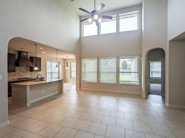 kitchen with arched walkways, custom exhaust hood, decorative backsplash, an island with sink, and pendant lighting