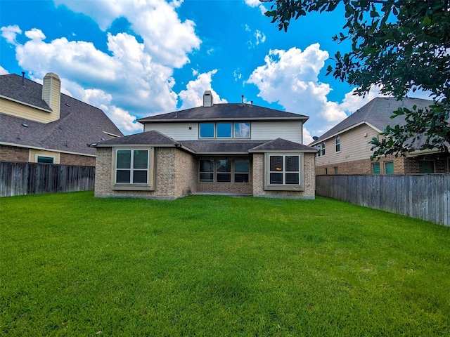 back of property with a fenced backyard, a chimney, a lawn, and brick siding